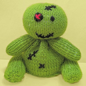 May include: A green knitted voodoo doll with a stitched-on mouth, black eyes, and a red X over one eye.