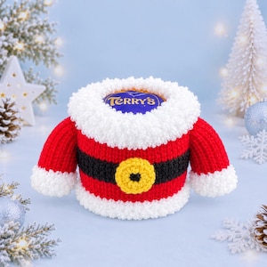 May include: A crocheted Santa-themed cover for a Terry's chocolate orange, featuring a red body, a black belt with a yellow buckle, and white textured trim around the collar, cuffs, and base, designed to fit snugly around the round chocolate.