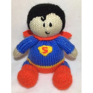 May include: A knitted toy doll dressed as Superman. The doll has a blue and red costume with a yellow 'S' on the chest. The doll has black hair and a white face.