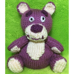 May include: A purple knitted teddy bear with white accents. The bear has a stitched-on smile and large, round eyes.