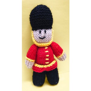 May include: A knitted toy soldier wearing a red and yellow uniform with a black hat.