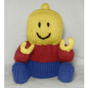 May include: A knitted toy resembling a Lego figure. The toy is yellow with a red torso and blue legs. It has a smiling face with black eyes and a black mouth.