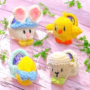 Peut inclure: Quatre décorations de Pâques tricotées. Un lapin blanc avec des oreilles roses et un chapeau bleu, un poussin jaune avec des pieds orange, un œuf jaune dans un panier et un agneau blanc avec un nœud papillon vert.