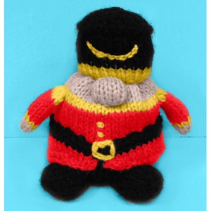 May include: A knitted toy gnome wearing a red and black uniform with gold accents. The gnome has a black hat with a gold trim and a gray beard.