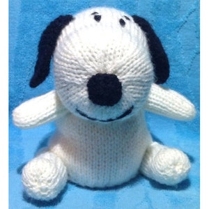 May include: A handmade, knitted dog toy in white with black ears, nose, and eyes. The plush dog has a round body, small arms, and legs. The toy is sitting on a blue surface.