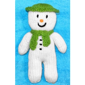 May include: A white knitted snowman with a green hat and scarf. The snowman has a black button nose and black eyes.