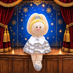 May include: A knitted doll with blonde hair, a silver crown, and a white dress featuring silver ruffled trim. The doll has black bead eyes, a pink stitched mouth, and a pearl necklace. It wears silver knitted ballet slippers with crisscross laces.
