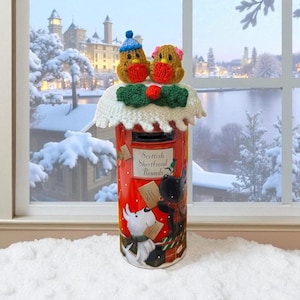 Könnte beinhalten: Ein roter Briefkasten mit einem dekorativen Strickaufsatz mit zwei Vogelfiguren. Der Briefkasten hat einen Schlitz für Post und Illustrationen von Hunden und Katzen. Der Text "Scottish Shortbread Rounds" ist sichtbar.