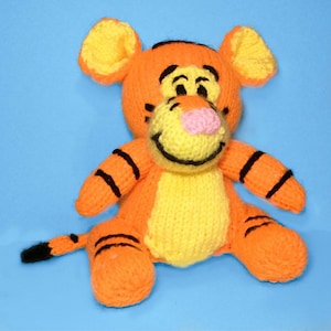 May include: A knitted orange and yellow stuffed tiger toy with black stripes. The toy has a pink nose and black eyes.