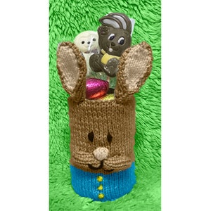 May include: A brown knitted bunny rabbit Easter basket with blue and yellow accents. The basket is filled with chocolate eggs and bunny-shaped candy.