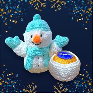Puede incluir: Un muñeco de nieve de crochet blanco sosteniendo un huevo de chocolate dorado y azul con la palabra "TERRY'S" en él. El muñeco de nieve lleva un gorro y una bufanda de punto azul. El fondo es azul oscuro con confeti dorado y azul.