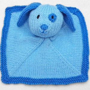 May include: A knitted baby comforter in shades of blue, featuring a dog's head with floppy ears and a dark blue spot. The square blanket has a darker blue border. The item is handmade.