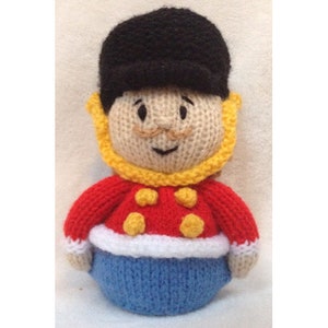 May include: A knitted toy soldier with a black hat, red jacket, yellow buttons, white trim, and blue pants.