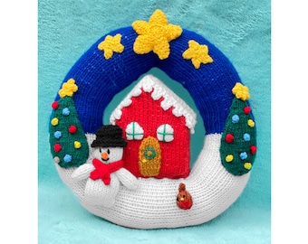 May include: A knitted Christmas wreath featuring a red house, a snowman, and two green Christmas trees. The wreath is blue and white with yellow stars.