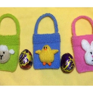 Peut inclure: Trois sacs à œufs de Pâques en tricot avec différents motifs d'animaux. Les sacs sont vert, bleu et rose. Chaque sac a un petit œuf en chocolat devant lui.