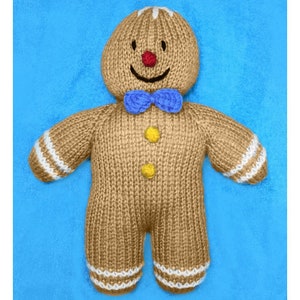 May include: A knitted gingerbread man toy with a blue bow tie, white icing details, and yellow buttons. The toy is brown and has a smiling face with red cheeks.