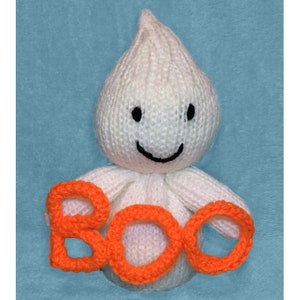 Pode incluir: Um fantasma de tricô branco com um rosto sorridente segura letras de tricô laranja que soletram "BOO".
