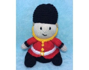 May include: A knitted toy soldier wearing a red and white uniform with a black hat. The toy has a yellow collar and a friendly face.