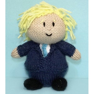 May include: A knitted doll with blonde hair, a blue suit, and a light blue tie. The doll has a smiling face with black eyes.