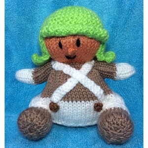 May include: A knitted gingerbread person doll with a green hat, brown body, white pants, and brown shoes.