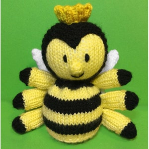 May include: A knitted bee toy with a yellow and black striped body, a yellow crown, and white wings. The bee has a smiling face with black eyes and a black nose.