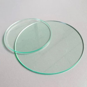 May include: Two clear glass circles, one smaller than the other, are stacked on top of each other. The circles are smooth and have a slight green tint.