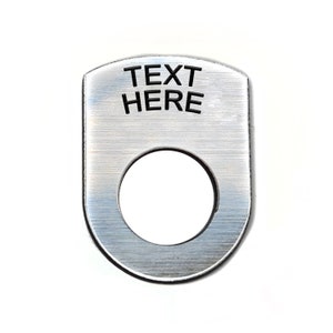 May include: A silver metal ring with a hole in the centre and the text "TEXT HERE" engraved on the top.