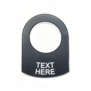 Pode incluir: Tampa de interruptor de bascula de plástico preto com um furo redondo e o texto "TEXT HERE" em branco.