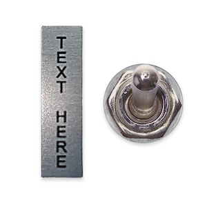 May include: A silver toggle switch with a metal plate that says "TEXT HERE" in black lettering.
