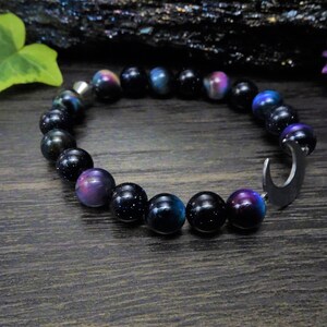 May include: A black and blue beaded bracelet with a crescent moon charm. The beads have a sparkly, iridescent finish.