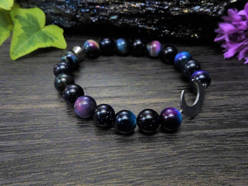 May include: A black and blue beaded bracelet with a crescent moon charm. The beads have a sparkly, iridescent finish.
