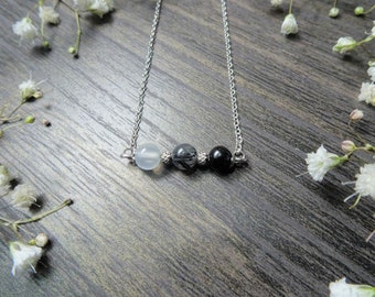 May include: A silver chain necklace with three beads: a white bead, a grey bead with black streaks, and a black bead.