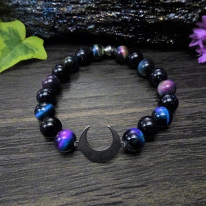 May include: A black beaded bracelet with a crescent moon charm. The beads have a dark blue and purple iridescent sheen.