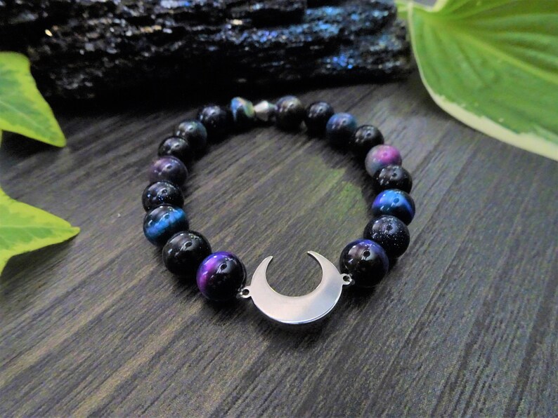 May include: A black beaded bracelet with a crescent moon charm. The beads have a galaxy-like iridescent shimmer.