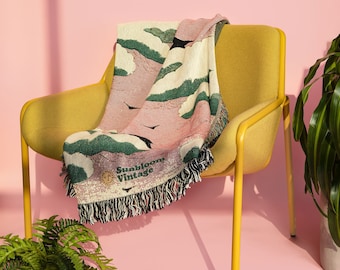 May include: A yellow chair with a pink and green woven throw blanket with the text "Sunbloom Vintage" on it. The chair is on a pink background.