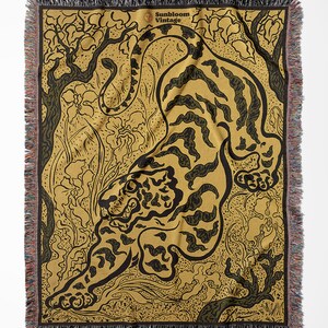 Pu&ograve; includere: Una coperta in tessuto di stile arazzo con un design di tigre nero e oro su uno sfondo di foresta verde e marrone. La coperta ha un bordo a frangia e un'etichetta "Sunbloom Vintage" nell'angolo in alto a destra.
