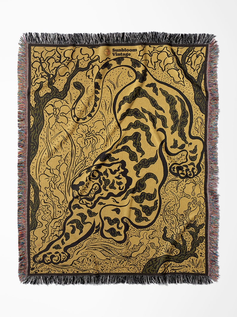 Pu&ograve; includere: Una coperta in tessuto di stile arazzo con un design di tigre nero e oro su uno sfondo di foresta verde e marrone. La coperta ha un bordo a frangia e un'etichetta "Sunbloom Vintage" nell'angolo in alto a destra.