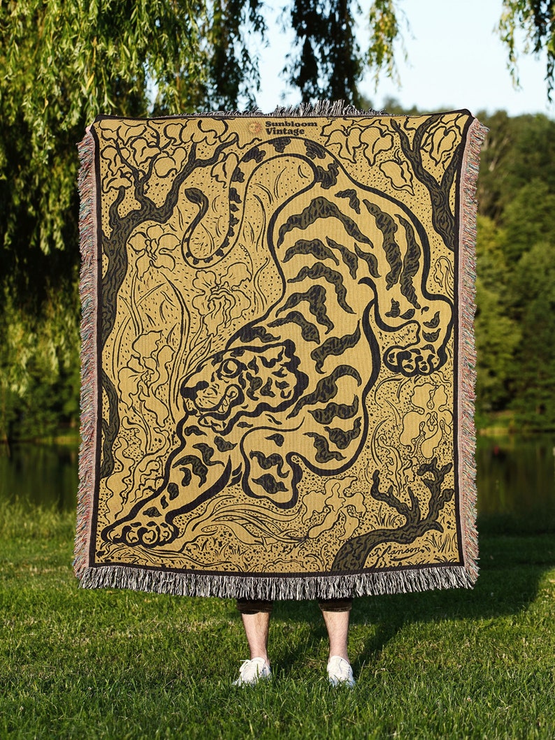 Pu&ograve; includere: Una coperta in tessuto di arazzo con un'illustrazione in bianco e nero di una tigre su uno sfondo giallo. La tigre &egrave; raffigurata in una posa dinamica, con la coda avvolta attorno al suo corpo. Lo sfondo presenta un motivo floreale stilizzato. La coperta ha un bordo a frange.
