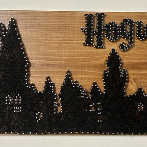 May include: Wooden sign featuring a black string art silhouette of Hogwarts castle with the word "Hogwarts" above it. The sign is made of stained wood and has a rustic appearance, perfect for fans of the wizarding world.