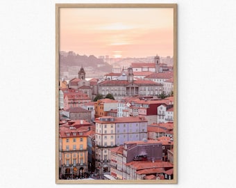 May include: A panoramic view of a city skyline with a pink and orange sunset in the background. The city is made up of many buildings with red tile roofs.