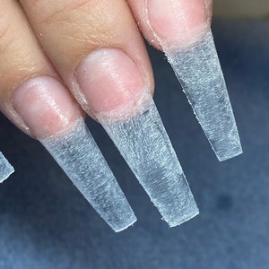 Könnte beinhalten: Nahaufnahme von fünf klaren, durchsichtigen Nagelspitzen mit einer strukturierten Oberfläche. Die Spitzen sind lang und schmal, mit abgerundeter Kante.