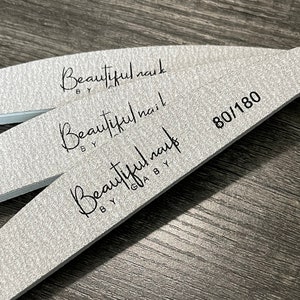 Peut inclure: Trois limes à ongles argentées avec le texte "Beautiful nail by Gaby" imprimé dessus. La lime du dessus porte la mention "80/180".
