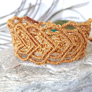 Peut inclure: Un bracelet en macramé doré avec un design délicat et complexe. Le bracelet est fait avec un cordon épais et a un motif tissé.
