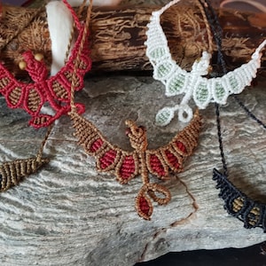 May include: Four macrame necklaces featuring a phoenix design. The necklaces are crafted with different coloured cords, including black, red, brown, and white.