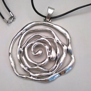 May include: A silver pendant necklace with a large, circular, openwork design resembling a rose. The pendant is attached to a black cord.