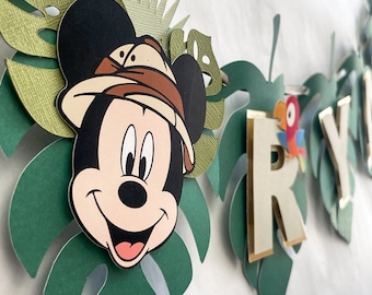 May include: A green and gold jungle-themed banner with a Mickey Mouse character wearing a safari hat. The banner has the letters "RY" in gold and white.