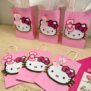May include: Pink Hello Kitty favor bags with gold trim and pink bows. The bags have a thank you tag with the text "Thank you for celebrating with us".