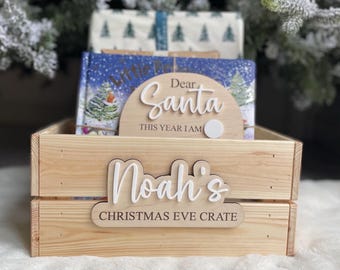 Pode incluir: Caixa de madeira com uma placa personalizada que diz "Noah's Christmas Eve Crate". A placa é branca com letras pretas. Há uma placa menor que diz "Caro Papai Noel Este Ano Tenho" com um círculo branco para a criança escrever sua idade.