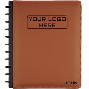 Pode incluir: Um caderno de couro castanho com encadernação em espiral preta. A capa apresenta o texto "YOUR LOGO HERE" numa caixa retangular e o nome "JOHN" na parte inferior. O caderno foi concebido para personalização.