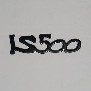 May include: Black, glossy emblem with the text "LS500" in a stylized font. The letters are connected, creating a sleek, modern design. The emblem is likely for a vehicle.